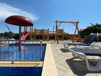 a pool with a playground with chairs and an umbrella at Imperial Family Bungalows in Ulcinj