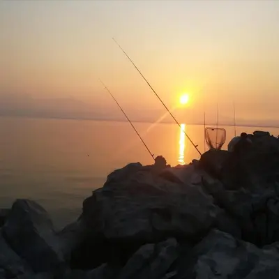 a person fishing on the rocks with the sunset in the background at Apartments Pajo in Vranjina