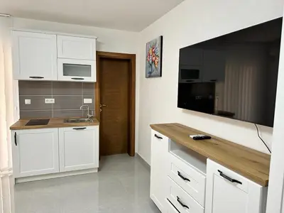 a kitchen with white cabinets and a flat screen tv at Студия, 800 м до моря in Bar
