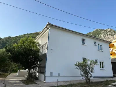 a white house with a mountain in the background at Apartmani Aki 1 in Sutomore